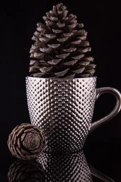 Pimpled silver coffee cup with a large pinecone inside on the reflective blac Stock Photos