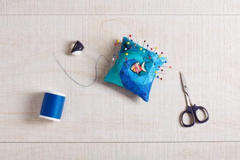 Pin cushion, scissors, spool of thread, thimble on cream-white wooden surface 스톡 사진