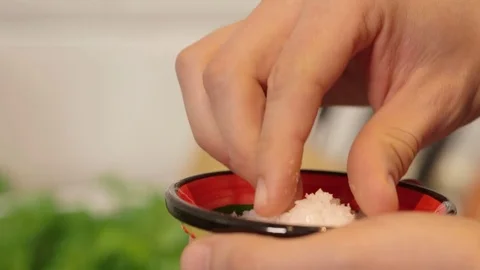 A pinch of salt in the kitchen, defocussed herbs and knives in background. Video stock 79836079