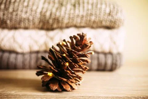 Pine cone with lights against stack of warm knitted sweaters Stock Photos