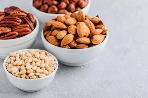 Pine nuts, almonds, pecans and hazelnuts in white bowls on grey background. M Stock Photos