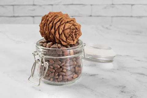 Pine nuts in a jar and a pine cone in the kitchen on a light background. Stock Photos