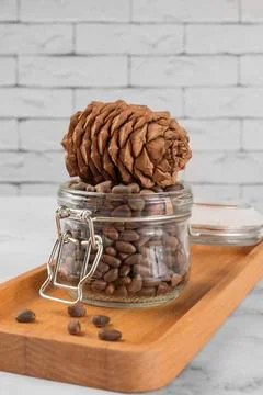Pine nuts in a jar and a pine cone in the kitchen on a light background. Foto stock