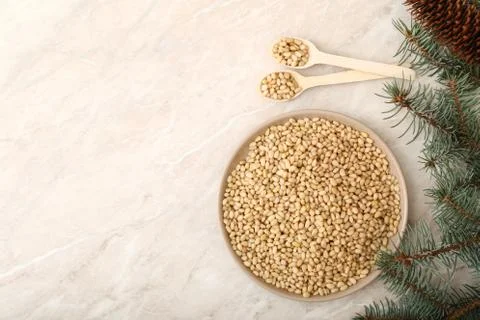 Pine nuts on the plate with two spoons, cones, brunches . top view on beige m Foto stock