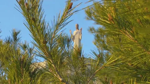 Pine tops swaying in the wind, the statue of Christ between the branches. Stock Footage 92550963