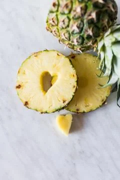 Pineapple and its slice with a heart shaped cut out lying on white background Stock Photos