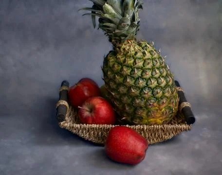 Pineapple in a basket with three red apples. Stock Photos