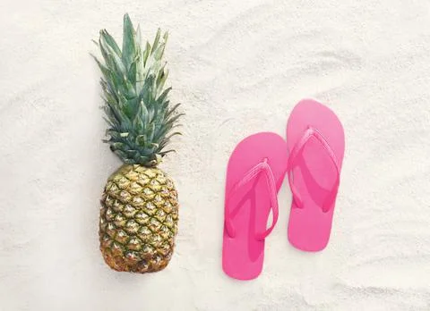 Pineapple fruit and pink flip flops on a beach white sand background, top vie Stock Photos