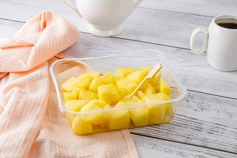 Pineapple fruit salad in a plastic container on a wooden background. Stock Photos