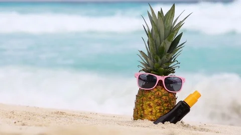 Pineapple fruit in sunglasses and sunscreen protection cream bottle on beach 스톡 동영상 69911259
