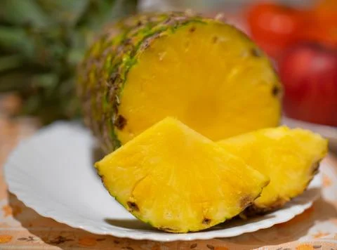 Pineapple fruit on white plate and red apples in the background Stock Photos