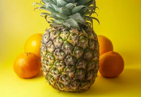 Pineapple isolated on yellow background with oranges and mandarin oranges. Sh Stock Photos