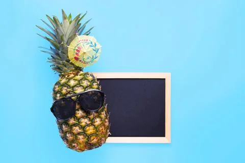 Pineapple in sunglasses with empty blackboard for your text on blue background Stock Photos