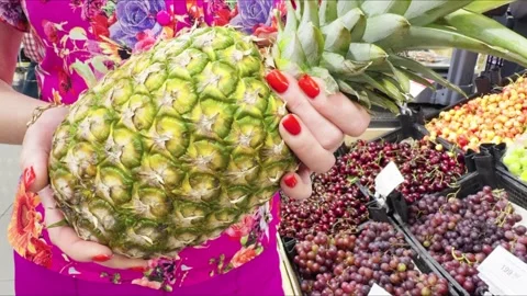 A pineapple in a womans hands against a fruit display window Stock Footage 311817347