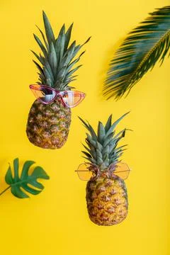 Pineapples creative faces in color sunglasses with palm leaves on yellow color Stock-Fotos