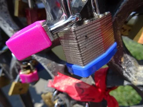 Pink and blue padlock fixed together on the fence over blurred background. Ro Stock Photos