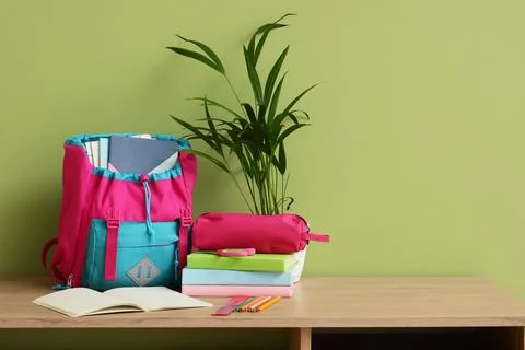 Pink and blue school backpack with books and stationery on a wooden desk agai Stock Photos