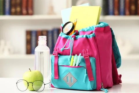 Pink and blue school backpack filled with books pencils and a magnifying glas Stock Photos