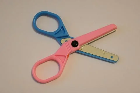 Pink and blue scissors on a plain surface Stock Photos