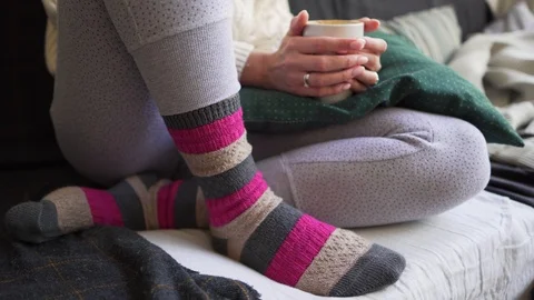 Pink and brown warm woolen socks close-up - a woman is sitting with a white cup Видео 114226442