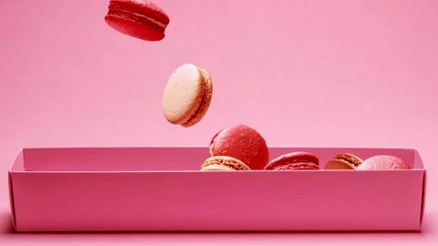 Pink and cream macarons falling into paper box on pastel background. Video stock 345112852