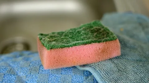 Pink and green sponge on a blue towel near the kitchen sink ready for cleaning Stock Footage 300959437