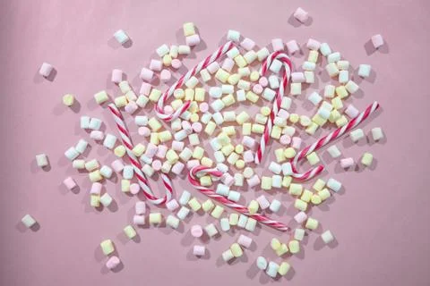 Pink background with a mix of tiny colored marshmallows and candy canes Stock Photos