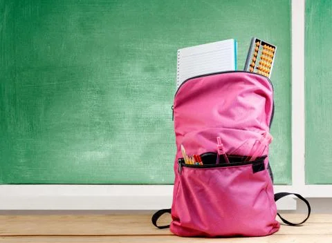 Pink backpack with book and different stationery on the wooden table Stock Photos