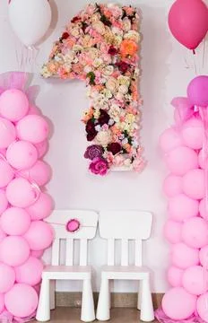 Pink balloon strings on either side of a large number one made of flowers Stock Photos