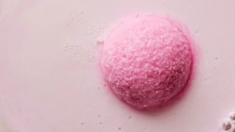 Pink bath bomb ball dissolves in water with white foam bubbles. Cosmetic product Stock Footage 147385117