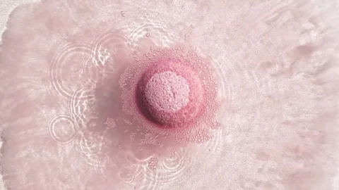 Pink bath bomb ball dissolves in water with white foam bubbles. Cosmetic product Stock Footage 253059987