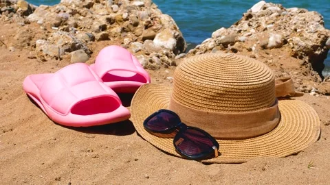 Pink beach clogs, straw hat and sunglasses on the sandy beach. In the background Stock Footage 247166014