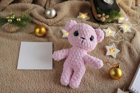 The pink bear lies on the table on a plush blanket. There is a wish card next to Stock Photos