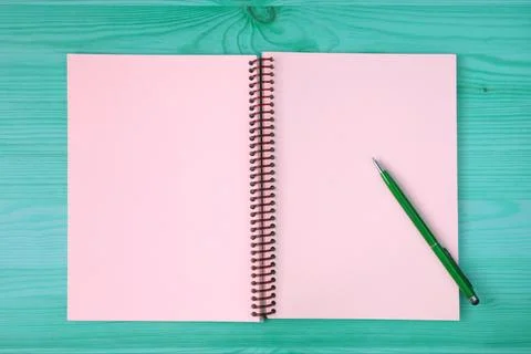 Pink blank page of an opened notebook and a green pen on the blue green table Stockfoto's