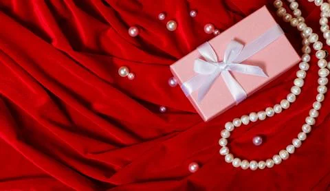 Pink box with a ribbon and a string of pearls on a red background. Stock Photos
