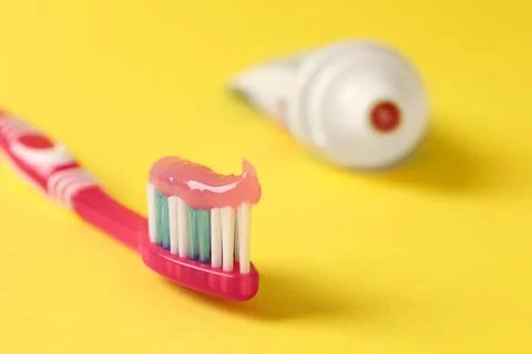 Pink brush with toothpaste on yellow background, closeup. Space for text Stock Photos