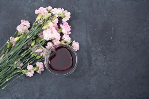 Pink carnations on a dark background with a cup of red tea in a heart-shaped cup Stock Photos