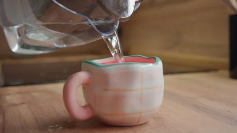 Pink ceramic mug filling from tilted glass pitcher with clear stream, gentle Stock Footage 343534558