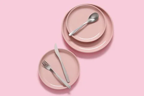 Pink ceramic plates with silverware on a solid pink background, minimalist ta Stock Photos