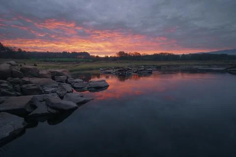 Pink clouds of dawn reflected in the river between the rocks Stock Photos