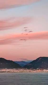 Pink clouds in evening sky over blue sea on background of city and mountains on Foto stock