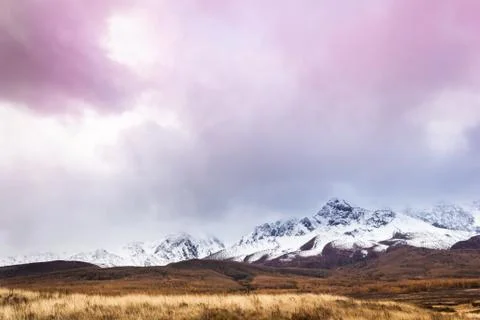 Pink clouds over mountain range. Rocks under snow on horizon. Sunset in mount