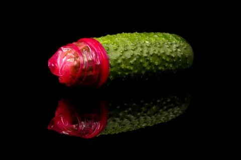 Pink condom pulled on cucumber isolated on the black Stock Photos