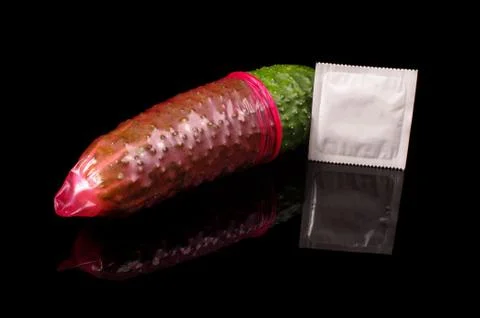 Pink condom pulled on cucumber isolated on the black Fotos de archivo