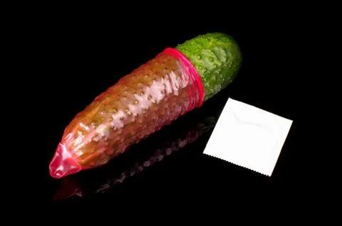 Pink condom pulled on cucumber isolated on the black Stock Photos