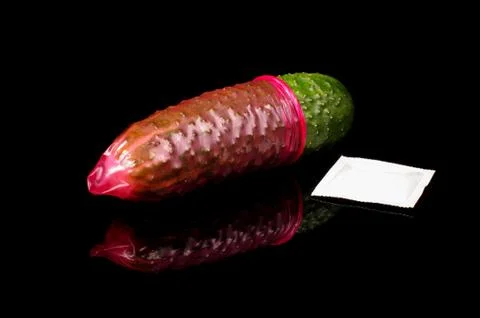 Pink condom pulled on cucumber isolated on the black Stock Photos