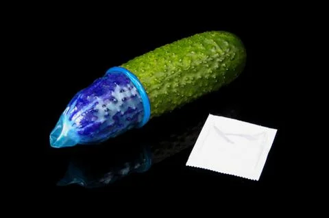 Pink condom pulled on cucumber isolated on the black Stock Photos