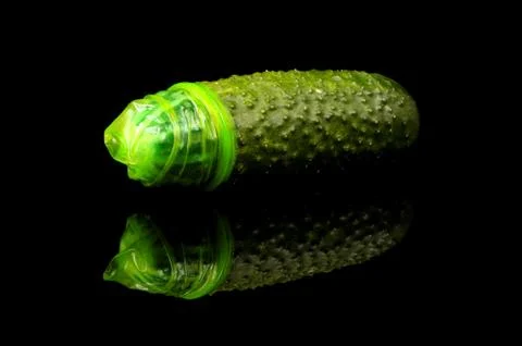 Pink condom pulled on cucumber isolated on the black Stock Photos