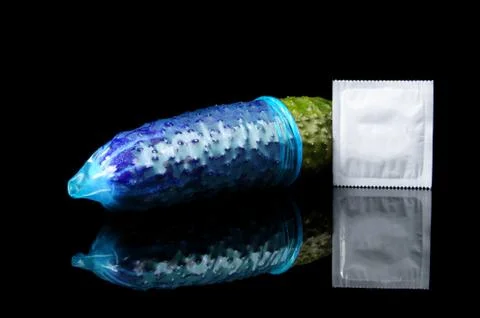Pink condom pulled on cucumber isolated on the black Stock Photos
