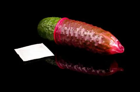 Pink condom pulled on cucumber isolated on the black Stock Photos